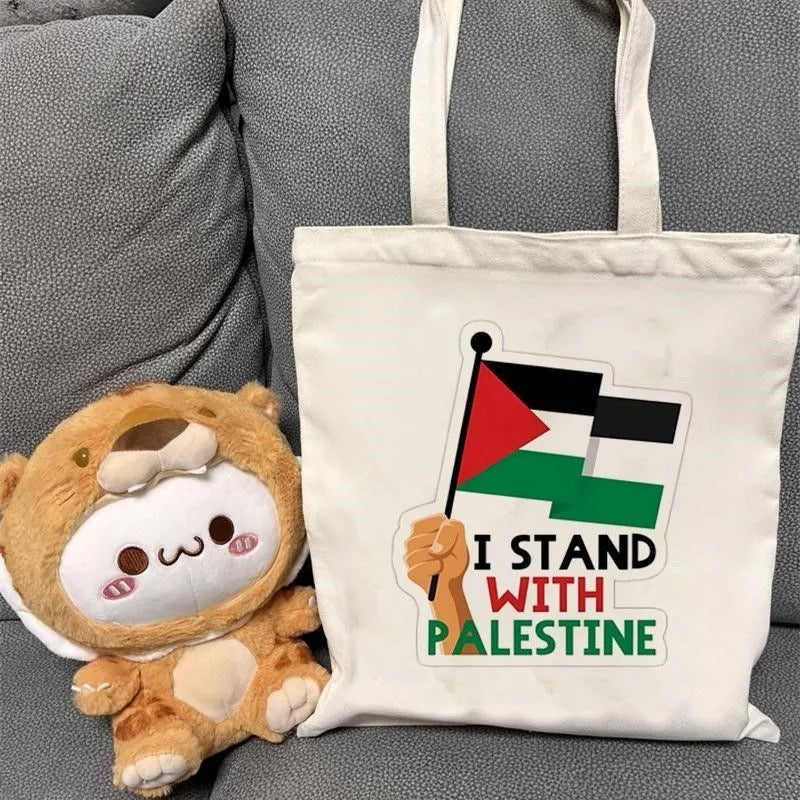 Hvid mulepose med teksten "I stand with Palestine" ved siden af en tøjbamse.
