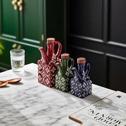 En stor rød, en lille grøn og en lille blå keramisk olivenolieflaske ved siden af hinanden