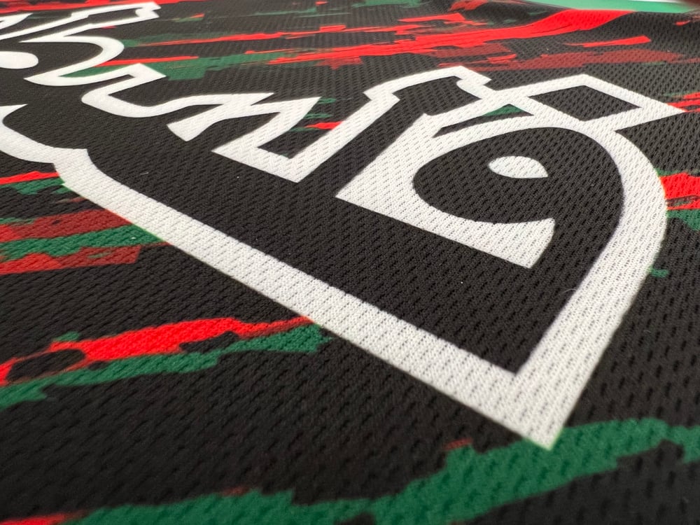 Tæt på billede af det hvide arabiske "Palæstina" tryk på brystet af sort trøje, der viser mesh-stoffets struktur.